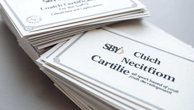 A close-up view of a neatly stacked pile of official-looking certificates labeled "SBYD Coach Certification", surrounded by a neutral gray background with a soft, subtle lighting. The certificates have a premium, high-quality appearance, with embossed logos and seals, conveying a sense of professionalism and legitimacy. The image evokes a feeling of achievement, recognition, and the successful completion of a specialized coaching program focused on sport-based youth development. A close-up view of a neatly stacked pile of official-looking certificates labeled "SBYD Coach Certification", surrounded by a neutral gray background with a soft, subtle lighting. The certificates have a premium, high-quality appearance, with embossed logos and seals, conveying a sense of professionalism and legitimacy. The image evokes a feeling of achievement, recognition, and the successful completion of a specialized coaching program focused on sport-based youth development.
